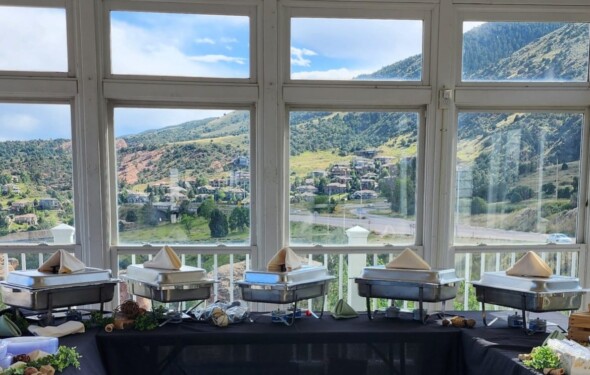 Buffet setup with chafing dishes in a room with large windows, overlooking a scenic mountain and town view.