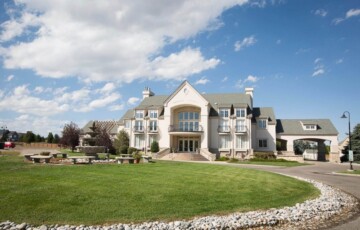 Large suburban house with manicured lawn and circular driveway under a blue sky with clouds.