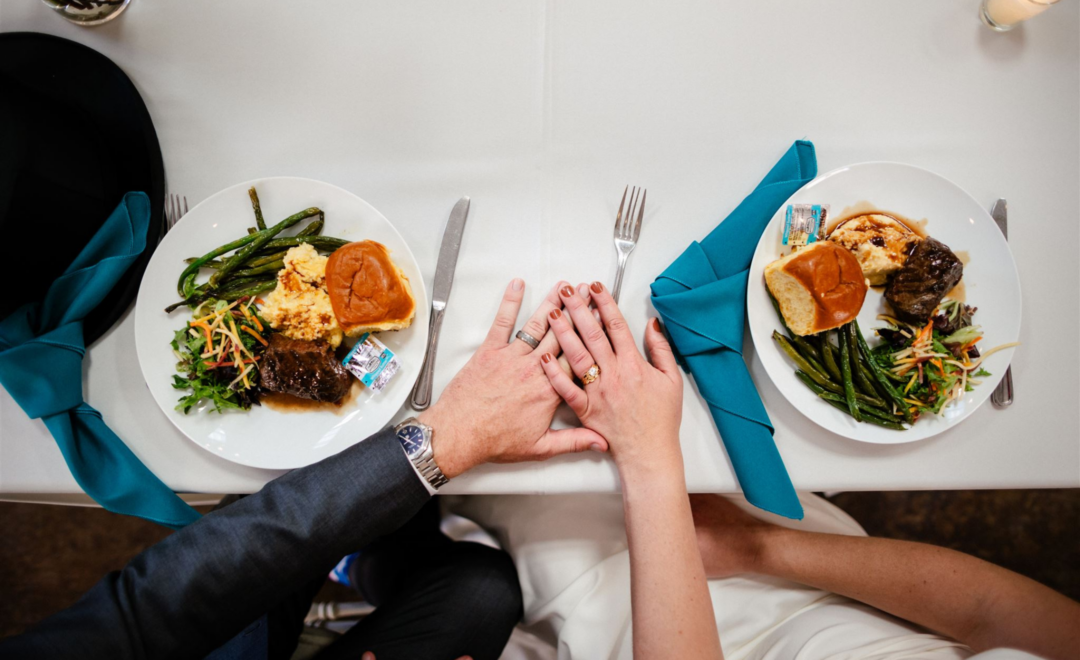 Couple holding hands over a table with two plates of food and teal napkins.