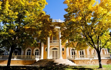 Historic building with tall columns surrounded by autumn trees under a clear blue sky.