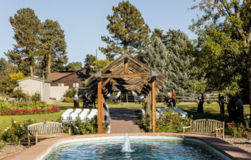 A wedding arch and seating setup in a garden with a fountain in the foreground and trees in the background.