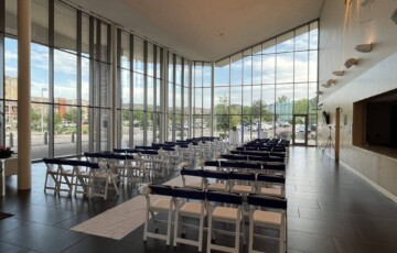 Modern hall with rows of white chairs and a long glass wall, set for an event with outdoor views.