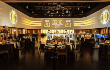 Elegant event hall with round tables, large digital scoreboard displaying 20:23, and sports-themed decor.