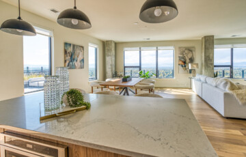 Modern open-plan living space with a kitchen island, dining table, and large windows offering city views.