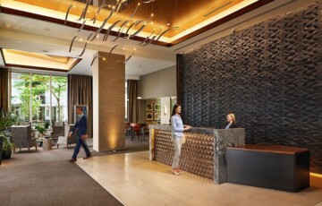 Modern hotel lobby with elegant design, featuring a woman at the reception desk and a man walking by.