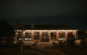 A building with outdoor string lights and people visible inside, set against a dark night sky.