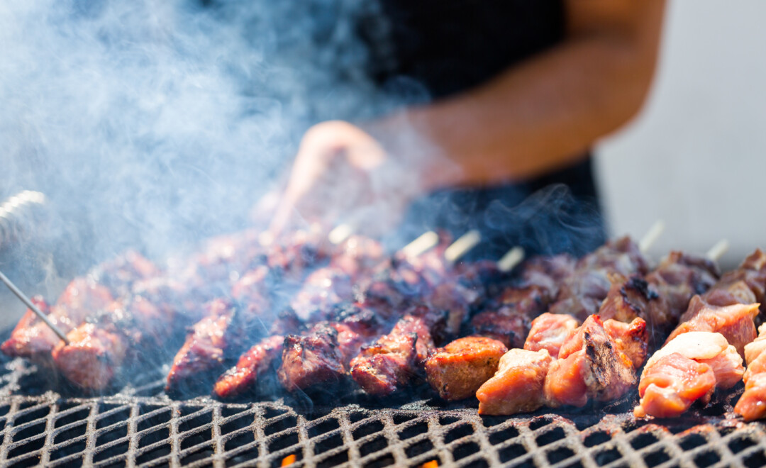 Person grilling skewered meat over a smoky barbecue grill at a Denver BBQ catering event.