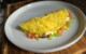 A folded omelette with tomatoes, green onions, and cheese on a white plate.