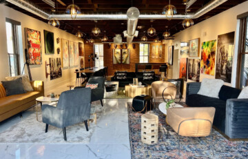 Modern art gallery with eclectic furniture, colorful paintings, and industrial-style ceiling lights.